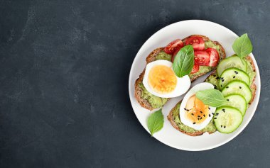 Sebzeli tost ekmeği, yumurta ve fesleğen siyah beton bir masada.