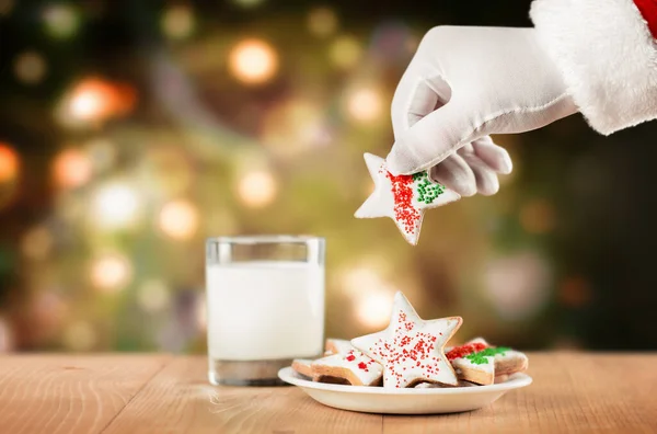 Noel Baba 'nın eli, Noel ağacının arka planındaki bir tabaktan kurabiye alır.