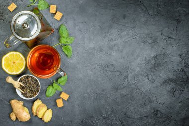Çay, limon, nane ve zencefil için malzemeler siyah bir masada, üst görünümde.