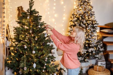 Çekici sarışın kız evde Noel ağaçları süslüyor.
