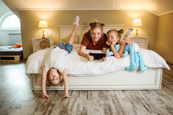 Anya és lányai jól érzik magukat otthon, és sorozatokat néznek a tableten.. Stock Kép