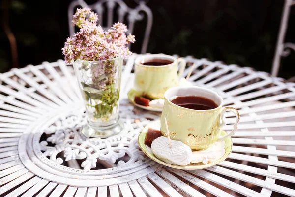 Two vintage cups of tea with sweets on the openwork table in the outdoor cafe. — Stock Photo, Image