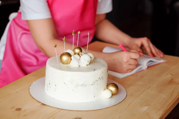 Lahodný narozeninový dort a ženské ruce psaní recept do sešitu na stole. — Stock fotografie