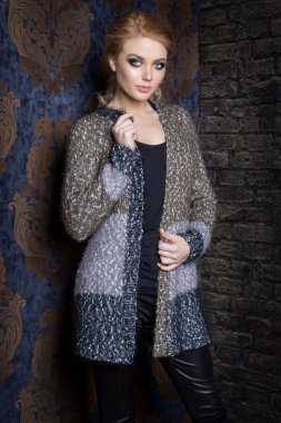 Uzun sarı saçlı güzel genç seksi kadın, parlak makyaj Smokey Eyes yanında bir kazak giyen bahar bir şifoniyer ve bir katalog giyim koleksiyonu sonbahar moda olan çubuk stili