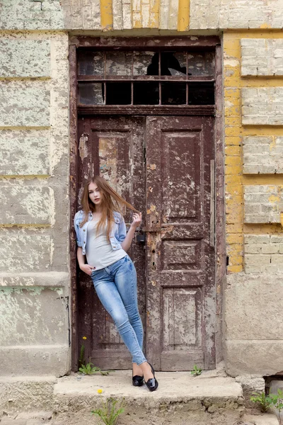 Красивая молодая милая девушка с рыжими волосами в джинсах, стоящая у дверей старого города — стоковое фото