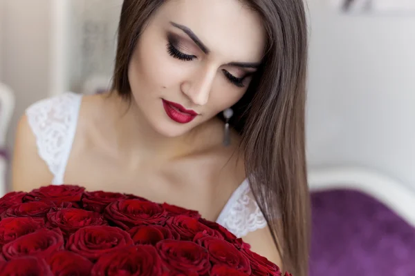 Schöne sexy devushkav weißen Morgenmantel mit einem großen Strauß roter Rosen in einem großen hellen Raum in der Nähe des Spiegels — Stockfoto