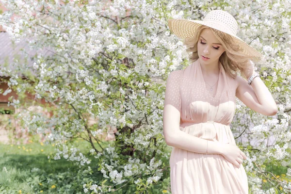 Bela menina encantadora doce em um chapéu de verão com uma maquilagem leve, com lábios cheios caminha no jardim florescente em um dia quente brilhante solnetsny — Fotografia de Stock