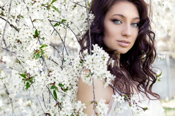 Potret seorang pengantin cantik seksi manis dengan mata lembut make-up bibir penuh dalam gaun putih berjalan di taman subur pada hari musim semi yang hangat — Stok Foto
