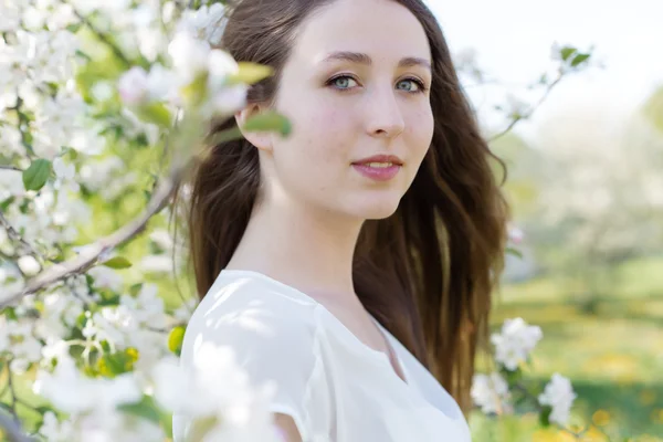 Vrij zoet tedere jong meisje met een lichte glimlach met lang blond haar onder de bloeiende appelbomen — Stockfoto