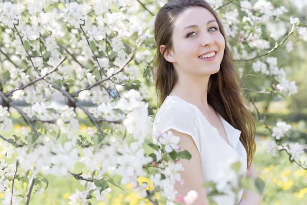 Chica joven tierna bastante dulce con una sonrisa brillante con el pelo largo y rubio entre los manzanos en flor — Foto de Stock