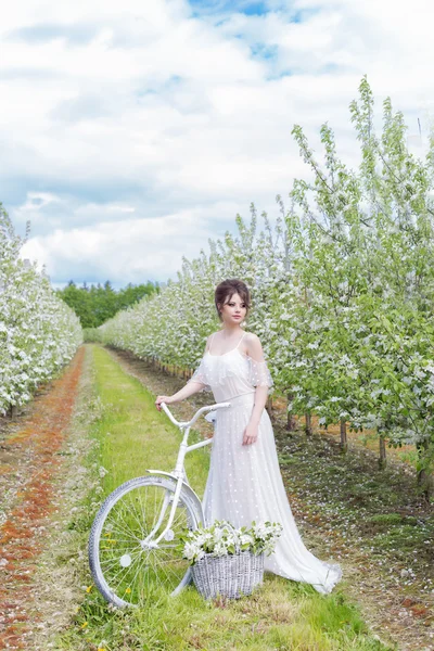 Güzel tatlı nazik mutlu elbiseli kız bej beyaz bir bisiklet ile bir boudoir ile çiçekli sepet, modern fotoğraf güzel sanatlar tarzında işleme — Stok fotoğraf