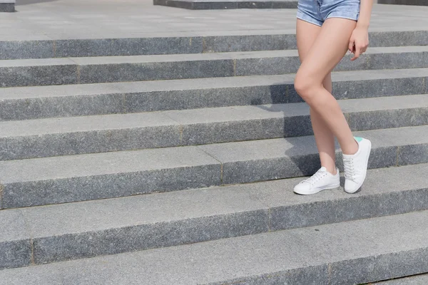Krásné, dlouhé nohy dívky v teniskách a džínové kraťasy na schodišti letní den — Stock fotografie