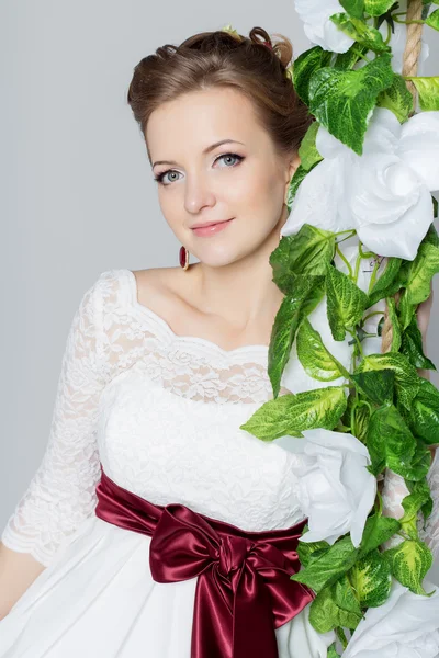 Bela noiva adorável está sentado em um balanço com um belo buquê de flores coloridas em um vestido branco com penteado à noite — Fotografia de Stock