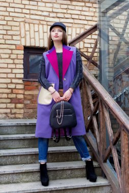 bir şapka ve parlak renkli ceket bir çanta ile uzun saçlı güzel mutlu sevimli kız şehrin içinden parlak güneşli bir günde yürür.