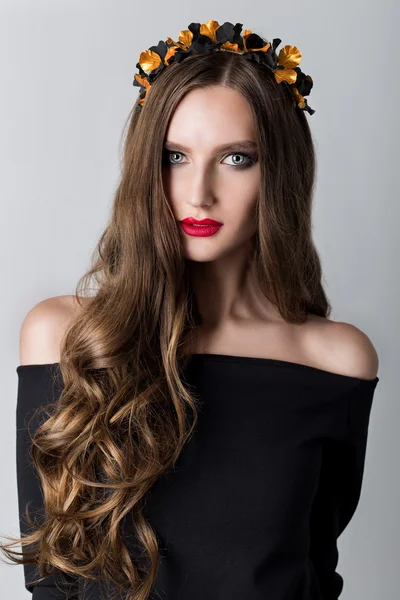 Beautiful cute skinny girl with long hair with a wreath on his head and bright make-up in elegant black dress with bare shoulders in the studio — Stock Photo, Image