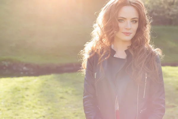 漂亮的红发女孩，在一件黑色的外套在小镇的公园阳光灿烂 — 图库照片