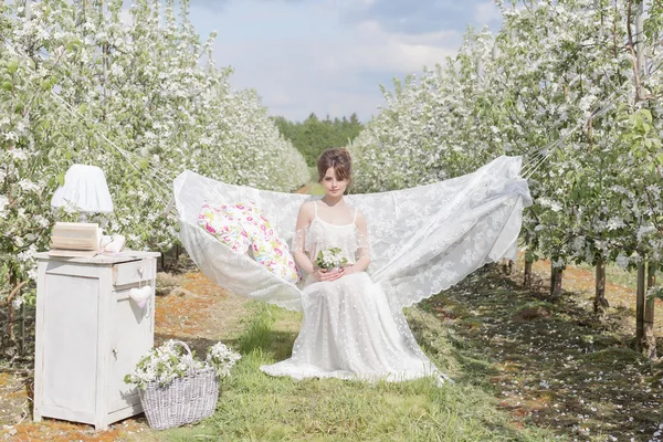 Elma Çiçek bahçesinde ışık beyaz elbiseli güzel seksi sevimli kız bir kitapla hamak görür — Stok fotoğraf