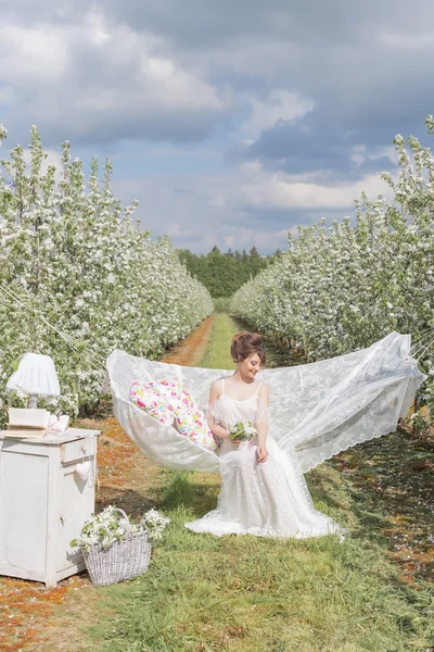 Elma Çiçek bahçesinde ışık beyaz elbiseli güzel seksi sevimli kız bir kitapla hamak görür — Stok fotoğraf