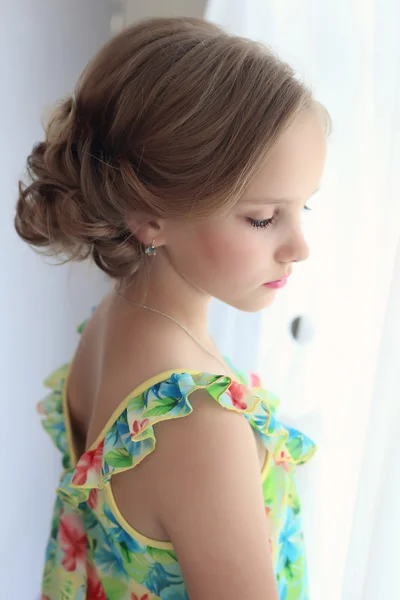 Linda menina doce com um penteado festivo com lábios e olhos pintados está perto da janela — Fotografia de Stock