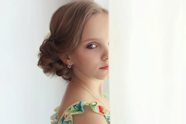 Beautiful little sweet girl with a festive hairstyle with painted lips and eyes is near the window — Stock Photo, Image