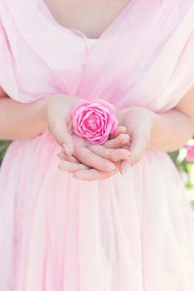 Menina sexy bonita em um vestido rosa, de pé no jardim em um dia de verão brilhante ensolarado detém uma rosa nas mãos — Fotografia de Stock