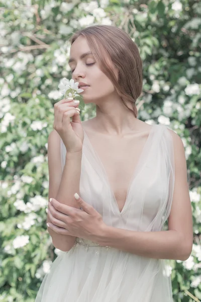 Hermosa novia chica sexy en un vestido ligero con maquillaje delicado y cabello en el jazmín jardín de flores. Estilo foto fane arte — Foto de Stock