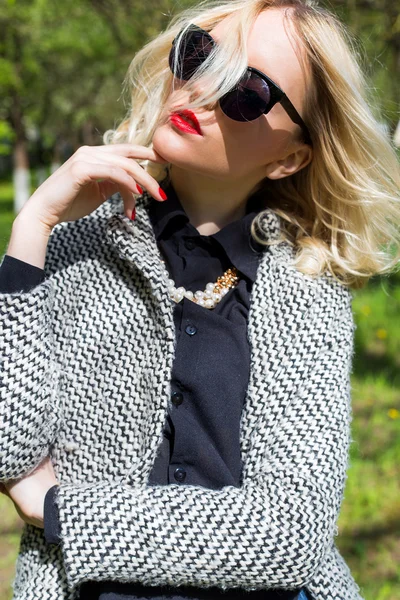 Beautiful sexy blond girl with red lips in sunglasses walking in the garden of a bright sunny day — Stock Photo, Image