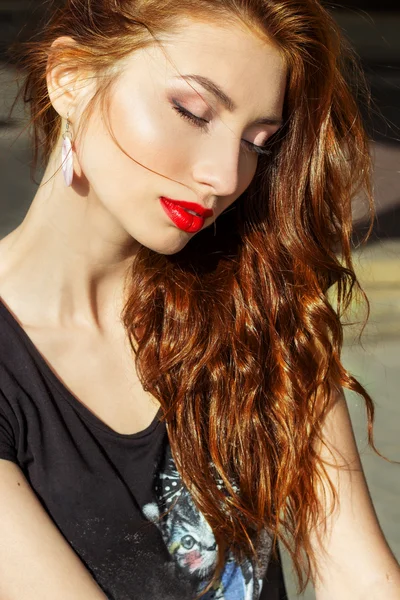 Schöne sexy Mädchen mit roten Haaren mit großen roten Lippen mit Make-up in der Stadt an einem sonnigen Sommertag — Stockfoto
