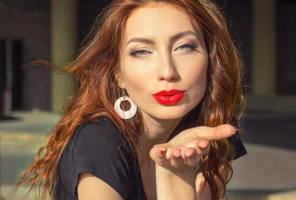 Hermosa chica sexy con el pelo rojo con grandes labios rojos con maquillaje en la ciudad en un día soleado de verano —  Fotos de Stock