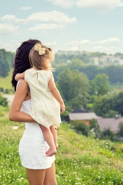 Young mother with a small daughter in his hands standing on the edge of the cliff and looks into the distance over the city on a summer day