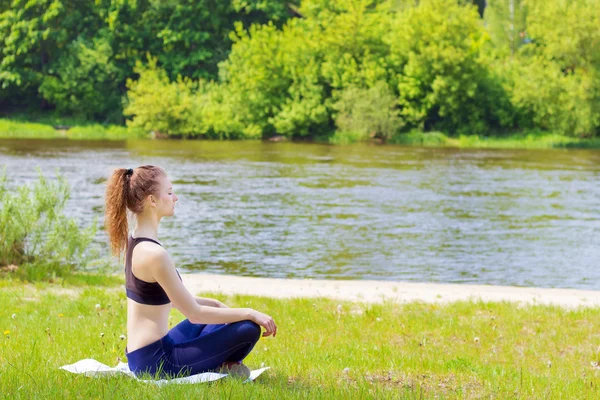 Piękna, młoda dziewczyna jest zaangażowany w Sport, joga, fitness na plaży nad rzeką w słoneczny letni dzień — Zdjęcie stockowe