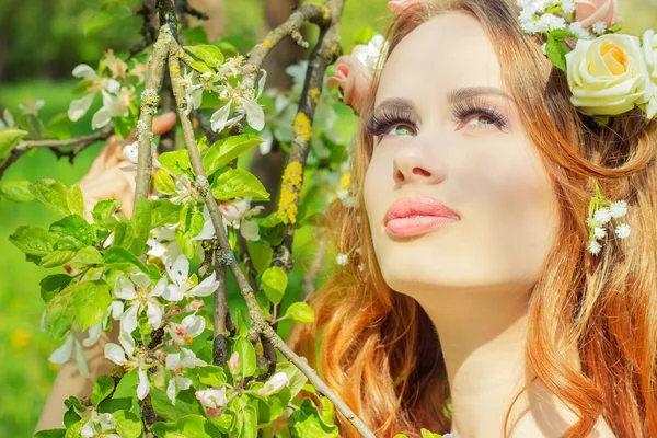 赤い髪と彼女の髪に花を持つ美しいセクシーな少女活気付くりんごの木のそばに立つ — ストック写真