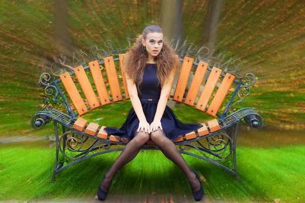 Bella ragazza giornata autunnale per strada con trucco di fantasia in un vestito nero con grandi labbra sexy seduto su una panchina nel parco — Foto Stock