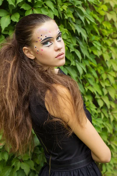 Schöne junge Mädchen auf dem Hintergrund der Blätter im Herbst Tag auf der Straße mit Fantasie-Make-up in einem schwarzen Kleid mit großen sexy Lippen — Stockfoto