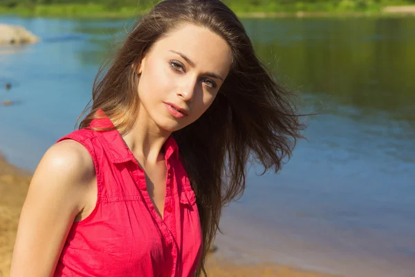 Sexy bella ragazza con lunghi capelli scuri seduto in pantaloncini di jeans sulla spiaggia in Sunny day — Foto Stock