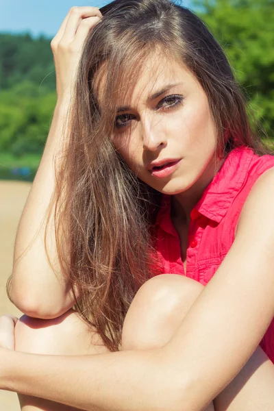 Sexy bella ragazza con lunghi capelli scuri seduto in pantaloncini di jeans sulla spiaggia in Sunny day — Foto Stock