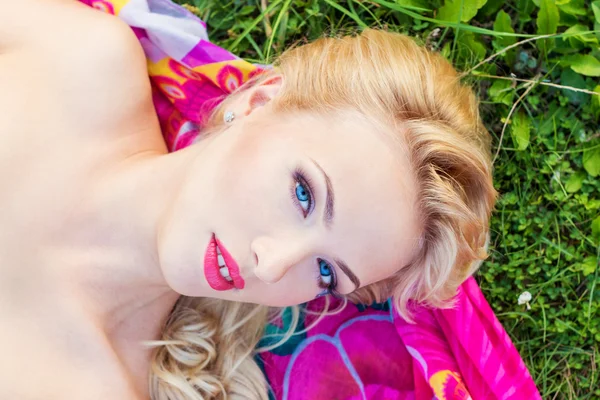 Beautiful sexy girl with bright makeup and red lips is lying on the grass on a warm summer day — Stock Photo, Image