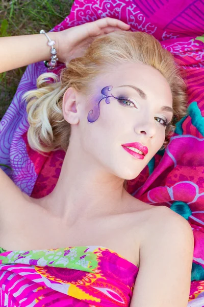 Beautiful sexy girl with bright makeup and red lips is lying on the grass on a warm summer day — Stock Photo, Image