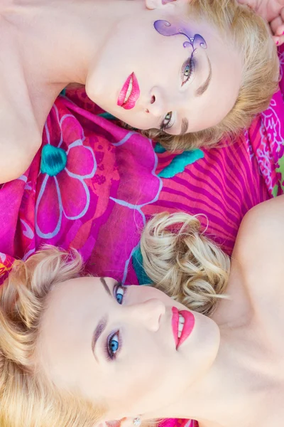 Hermosas chicas sexy, hermanas con maquillaje brillante y labios rojos se encuentran en una manta brillante en un parque en un cálido día de verano —  Fotos de Stock