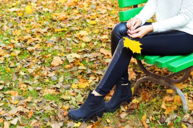 Güzel bacaklar kız siyah pantolon ve sarı yapraklar sonbaharda Park banktaoturuyor elinde ile çizme