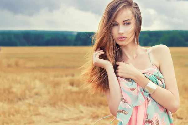 Beautiful sexy romantic girl with red hair wearing a colored dress, the wind standing in the field on a cloudy summer day — Stock Photo, Image