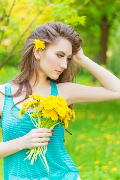 Belle fille dans une journée ensoleillée d'été marchant dans le jardin et garde les pissenlits jaunes dans les mains — Photo