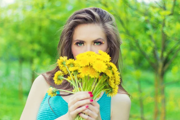 Hermosa chica en un día soleado de verano caminando en el jardín y mantiene dientes de león amarillos en las manos — Foto de Stock