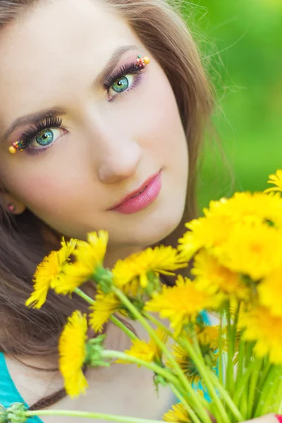 Belle fille dans une journée ensoleillée d'été marchant dans le jardin et garde les pissenlits jaunes dans les mains — Photo