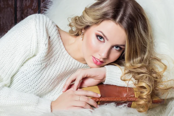 Beautiful smiling happy girl with bright makeup lies on the bed with fur in white sweater — Stock Photo, Image