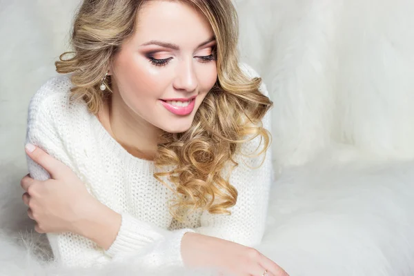 Beautiful smiling happy girl with bright makeup lies on the bed with fur in white sweater — Stock Photo, Image