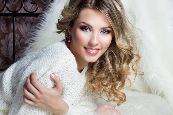 Beautiful smiling happy girl with bright makeup lies on the bed with fur in white sweater — Stock Photo, Image