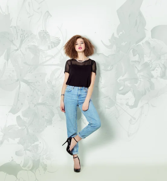Vacker sexig tjej i jeans och en svart t-shirt står nära en vit vägg, ljus makeup och frisyr, foto i Studio — Stockfoto