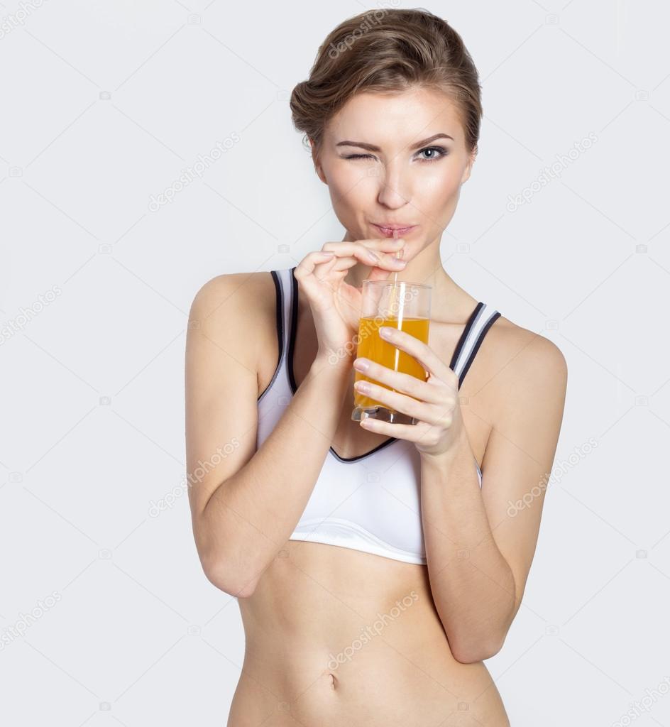 Sporting a beautiful young smiling girl with a glass of orange juice in his hands winks, healthy living, photography Studio on white background