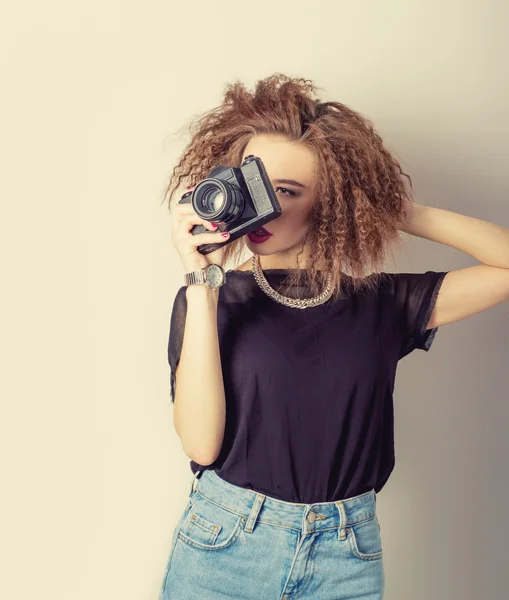 Красива молода сексуальна жінка в джинсах з камерою в руках кучерявого волосся в студії, ретро фільтр — стокове фото